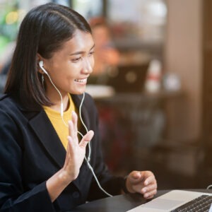 close up asian woman use earphone connect to laptop and talking greeting by video conference with friends or family at outdoor coffee restaurant in relax time , lifestyle people concept