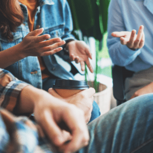 Close-up of a group of people engaged in a casual yet animated discussion, with hands gesturing and a coffee cup in view, symbolizing open and meaningful conversations.