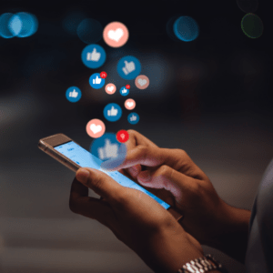 A woman's hands holding a smartphone with floating like and heart icons, indicating she is engaging on social media.