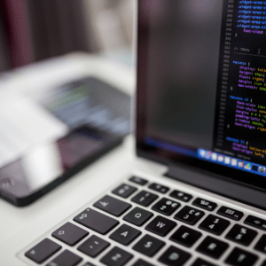 A laptop displaying lines of code on the screen, with a smartphone and blurred background, symbolizing programming and modern technology.